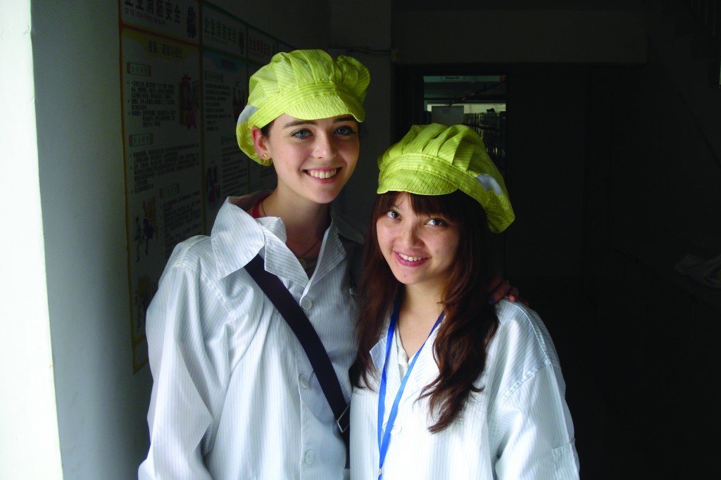 Heather Foye, FCLC ’14, and Janet, her Chinese roommate, pose in smocks and hats in an electronics factory. (Courtesy of Heather Foye)
