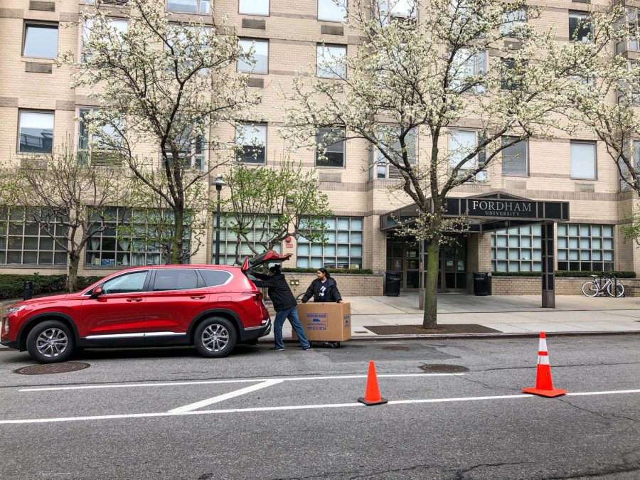 A red car with the rear hatch open as two people pack it with moving boxes in front of McMahon Hall