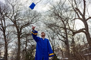 a student wearing a blue graduation gown and throwing a cap into the air