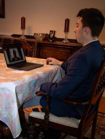 a student wears a suit while sitting at a kitchen table in front of an open laptop