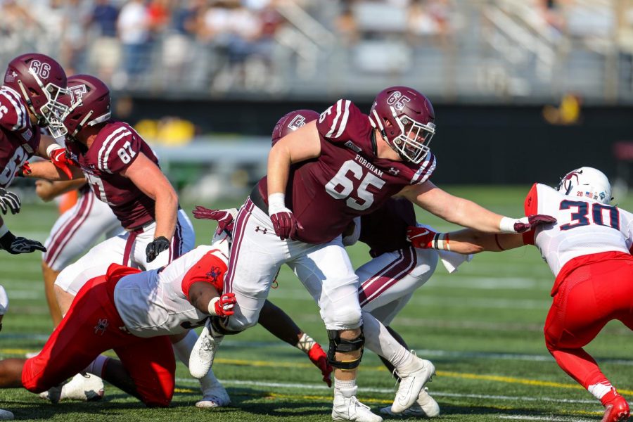 Fordham football player #65 reaches his arm out to block a member of the opposing team