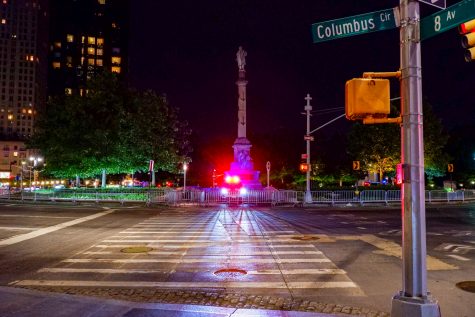 an NYPD cruiser with its lights on sits in front of the Columbus statue at night