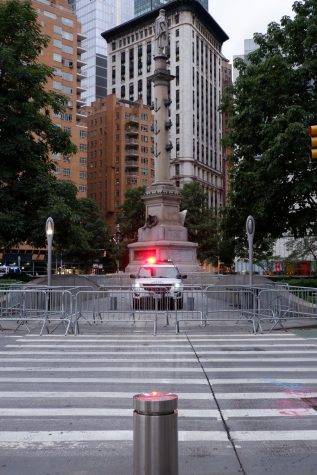an NYPD car guards Columbus Circle with one red light on in the center of the street behind a pedestrian barricade fence