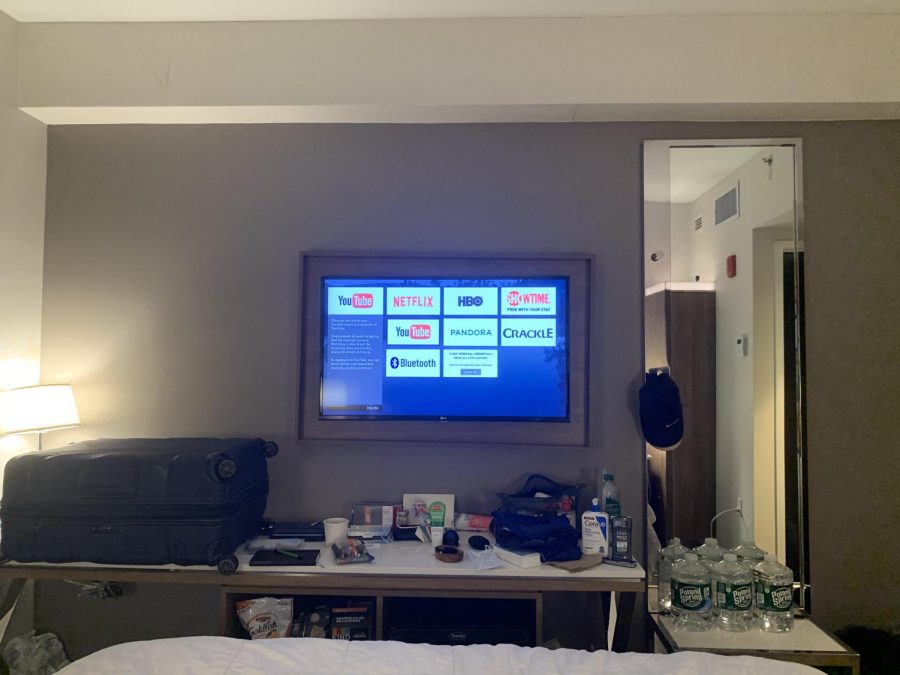 a+hotel+room%2C+including+a+TV+with+Netflix%2C+Crackle+and+YouTube+icons+on+it%2C+water+bottles%2C+a+table+and+a+couch