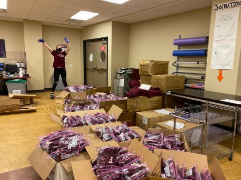 girl with gloves standing in front of boxes filled with maroon Fordham shirts for orientation