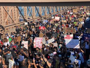 a large crowd of BLM protestors crossing a bridge while carrying signs