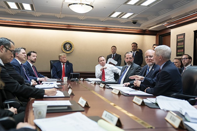 president and group of people sitting at a conference table discussing a vaccine