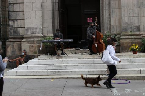 man playing upright bass at the top of a short church staircase, with a woman walking her dog in the foreground