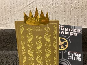 a gold copy of pride and prejudice with a gold crown on top of it, in front of a copy of the hunger games, which is supposedly less worthy to read
