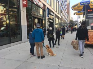 line of people standing on a sidewalk, including a dog