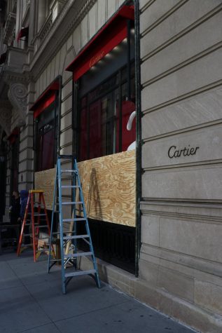 a ladder stands on the sidewalk as boards are put up on the windows of a Cartier store