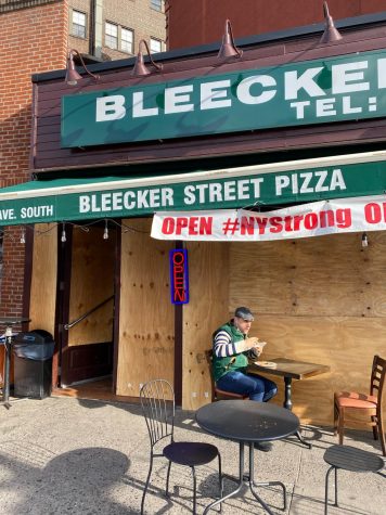 Bleecker Street Pizza with the windows boarded up and a patron eating a table outside