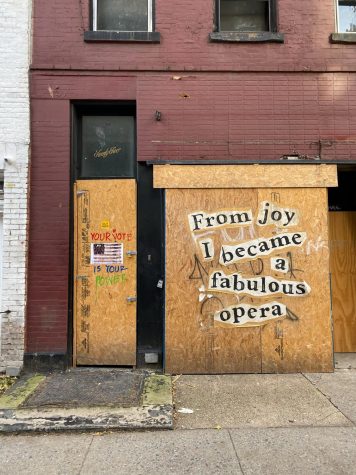 A boarded up building with the phrase "From joy I became a fabulous opera" stickered on the boards