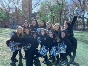 group of girls, fordhams dance team, on a football field with black uniforms and silver pom-poms
