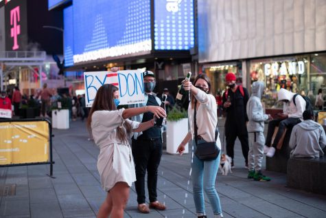 two people pop champagne bottles while someone stands behind them holding a sign reading "BYE DON"