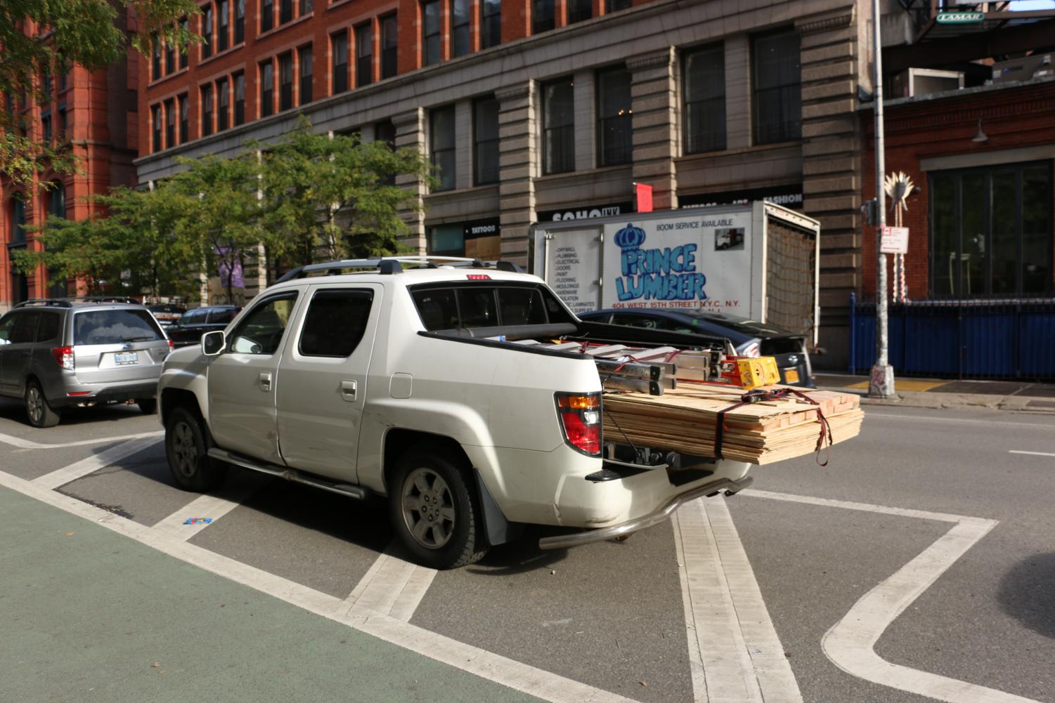 a pickup truck with the back filled with boards and ladders parked on the street