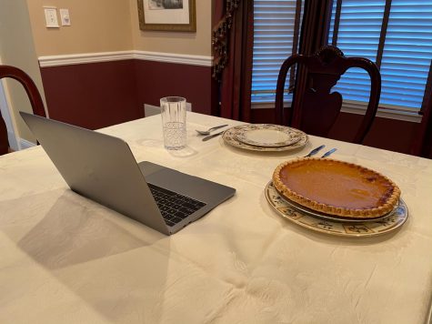 a laptop and pumpkin pie sit on a set dinner table