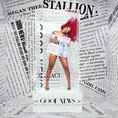 Megan the Stallion appears in a clear box with newspapers filling the background. The box she is standing on says Good News on the bottom of the platform.