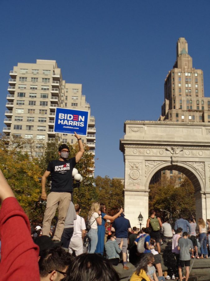 someone holds a Biden Harris sign in front of the Washington Square Arch