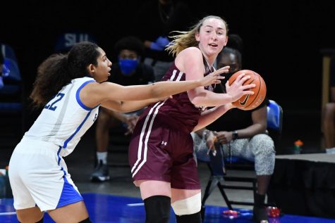 kaitlyn downey in a maroon uniform holding a basketball while a saint louis player, to the left of her in a white uniform, reaches over and tries to take it