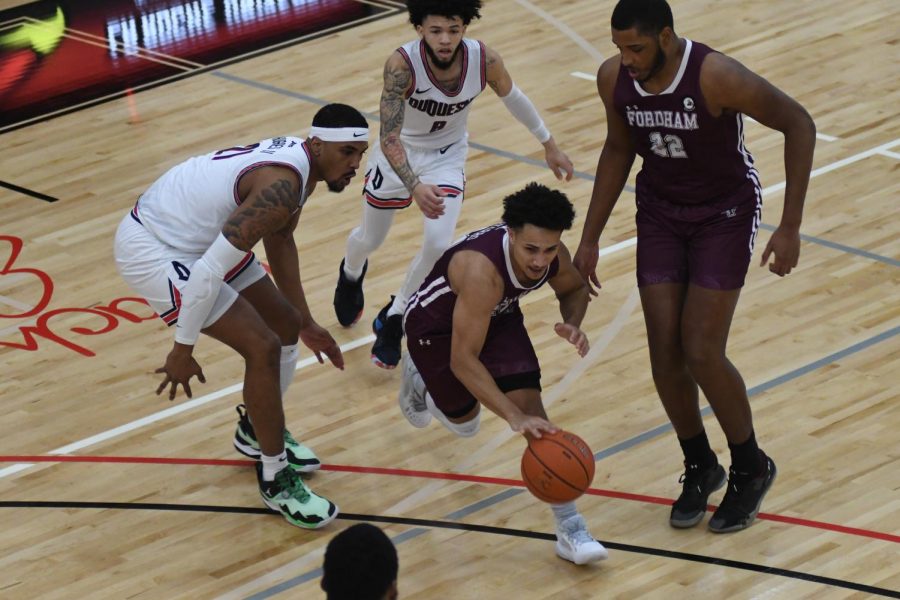 basketball player josh navarro dribbles a ball down a basketball court surrounded by one fordham player and two duquesne players