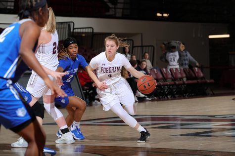 anna dewolfe dribbling a basketball down the court in the center of the photo, with two other players to the left