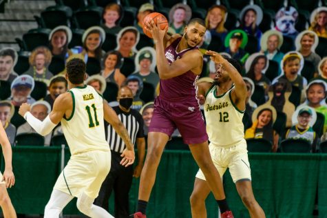 photo of a fordham player on the basketball court with a george mason player on either side of him