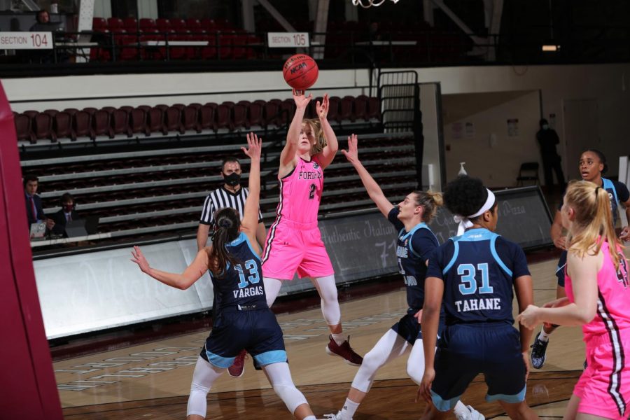 anna dewolfe jumping to make a basket in a game against URI. she is surrounded by three URI players in blue uniforms and one fordham player in a pink uniform