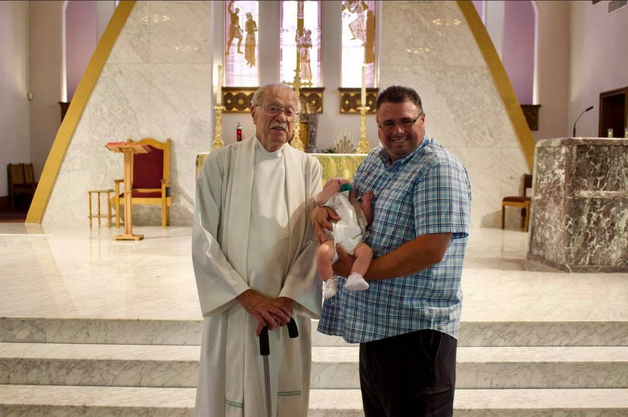 denniston standing next to a man holding a baby in a church