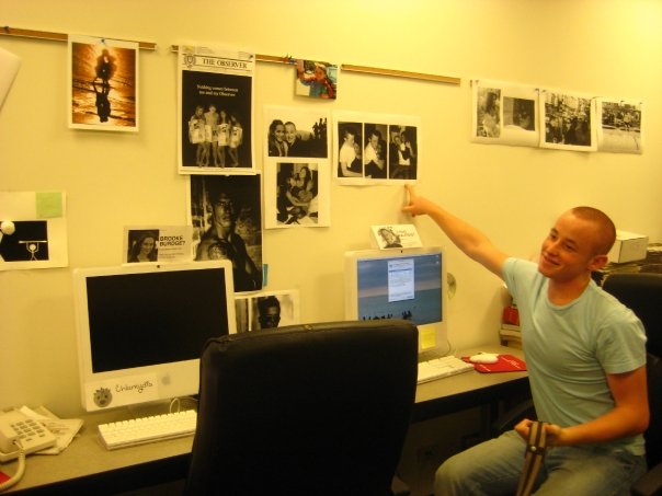 a young Craig Calefate sits in The Observer office and points to photos on the wall