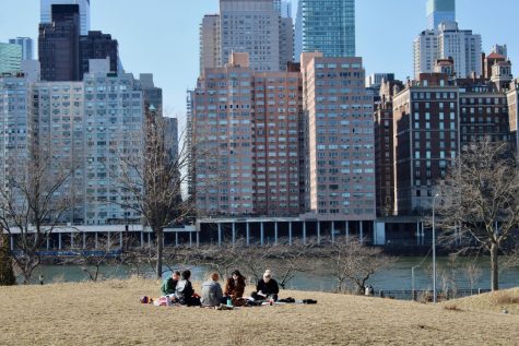 group of people having a spring picnic on the lawn of a park with a skyscraper in the background