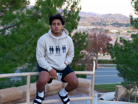 Juan Rodriguez sits on a railing while modeling a sweatshirt from his brand COHRTA
