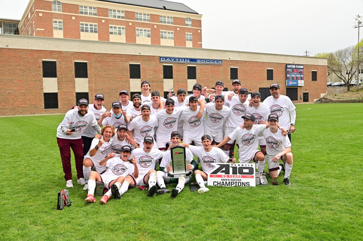 men's soccer poses on the grass with the A10 championship trophy