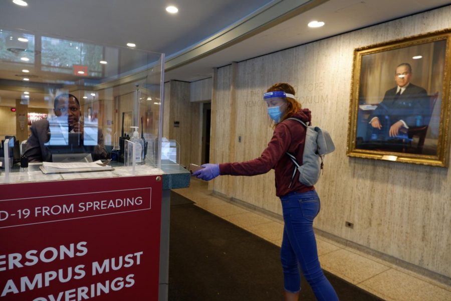 for an article about covid-19 photos, a student swipes their card to enter Fordham LC while wearing a mask, face shield, and latex gloves