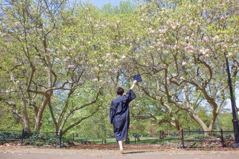 for an article about covid-19 photos, a student, facing away from the camera, carries their graduation cap wearing a gown in Central Park