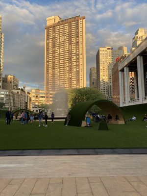 The GREENs arches covered in synthetic grass stand in front of the city skyline.