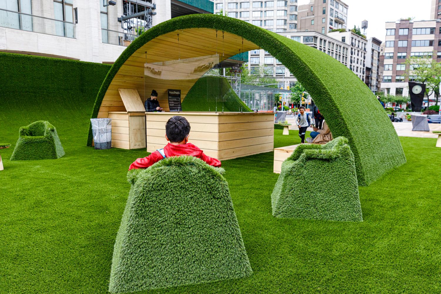 A child sits in a green grass chair in front of one of the grassy arches at The GREEN. 