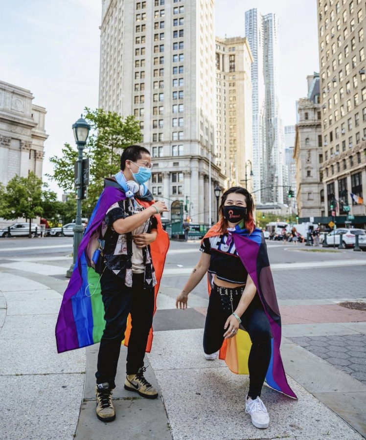 for an article about transgender housing on campus, two young people stand in NYC wearing pride flags on their backs