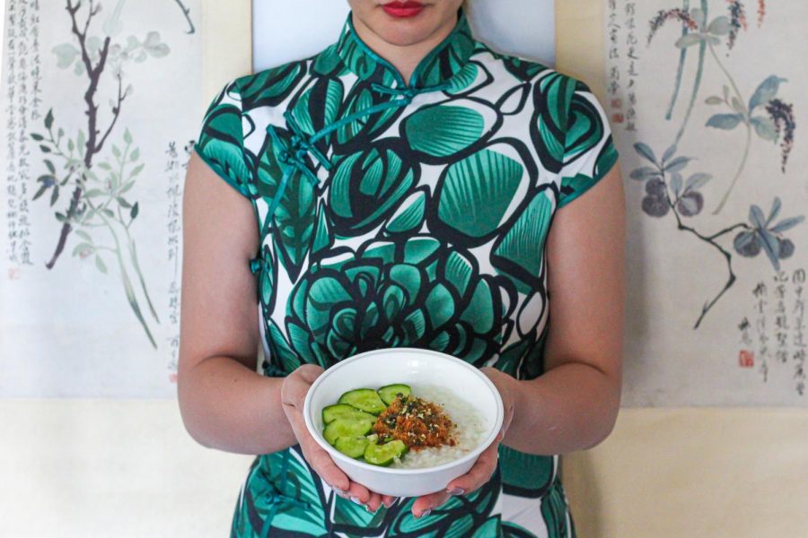 a woman in a green dress holds a bowl of congee made here in a Taiwanese style with garlic cucumbers and pork floss