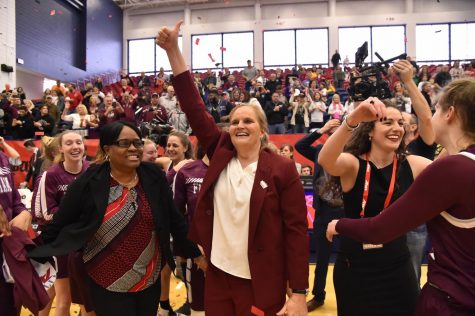 Sonia Burke stands next to Stephanie Gaitley. Both women are smiling and surrounded by the women's basketball team.