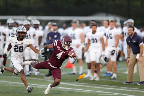 A Fordham football player catches a ball with one hand in front of many Monmouth players