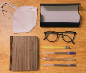 School supplies, glasses, and a mask laid out orderly on a wood table