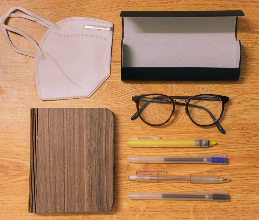 School+supplies%2C+glasses%2C+and+a+mask+laid+out+orderly+on+a+wood+table