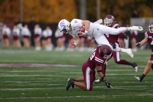 a fordham football player on his knees under a jumping holy cross football player