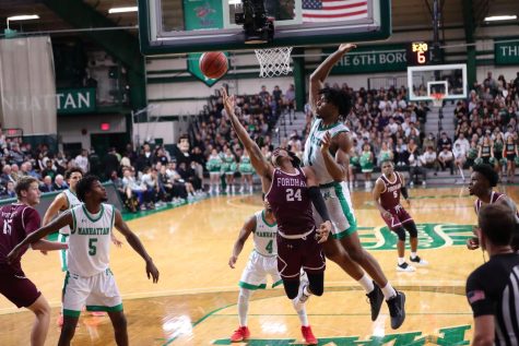 a fordham basketball player trying to score on a lay-up while being blocked by a Manhattan basketball player