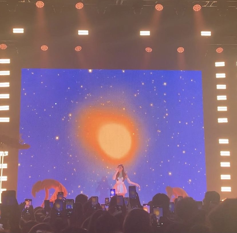 madison beer concert with blue background and orange circle behind singer
