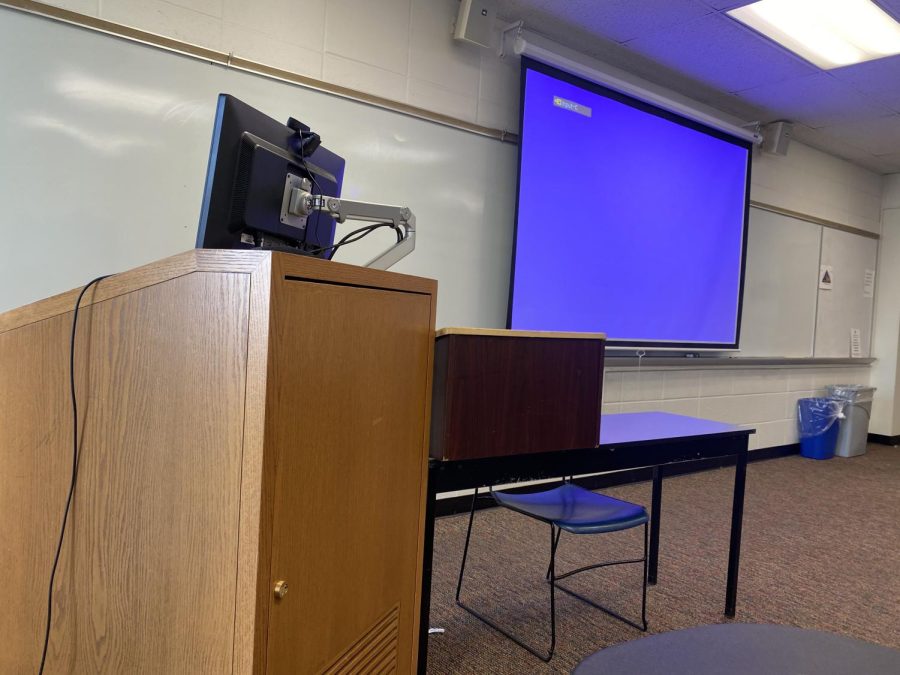 a classroom with a blue screen projector and an empty podium