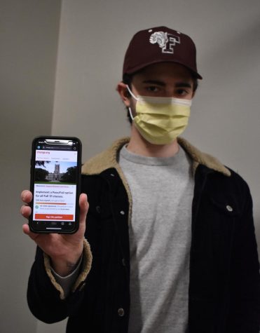 john lonie holds a phone with petition for pass/fail open on it, he wears a fordham hat and a mask