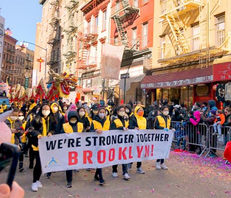 at lunar new year celebration, people hold a sign that reads we're stronger together brooklyn