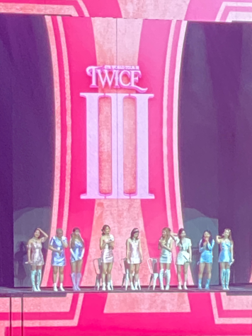 twice standing in front of a pink sign with twice and iii on it